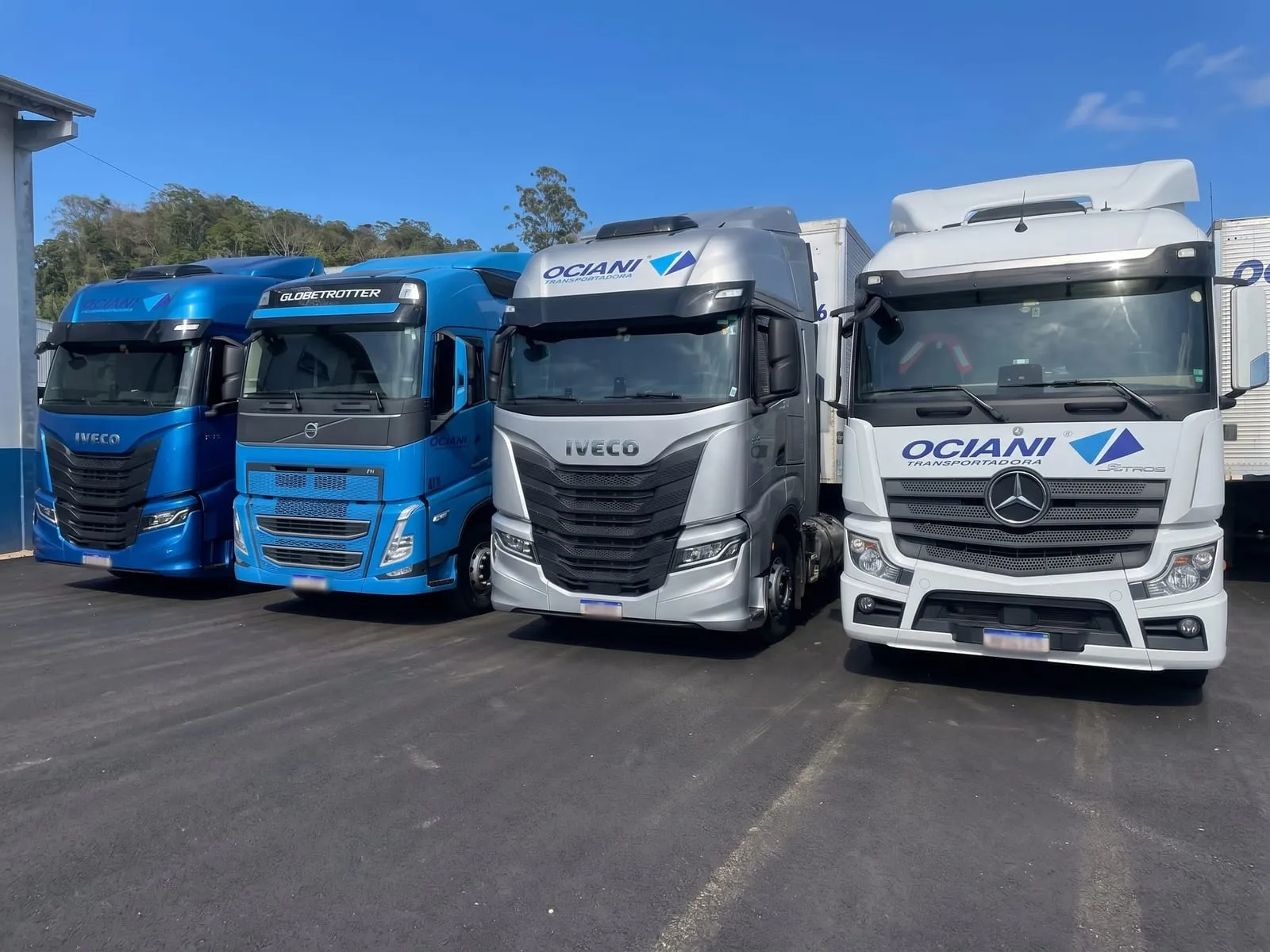 Quatro cavalos da Ociani lado a lado no pátio: Iveco S-Way azul, Volvo FH Globetrotter, Iveco S-Way prata e Mercedes-Benz Actros branco